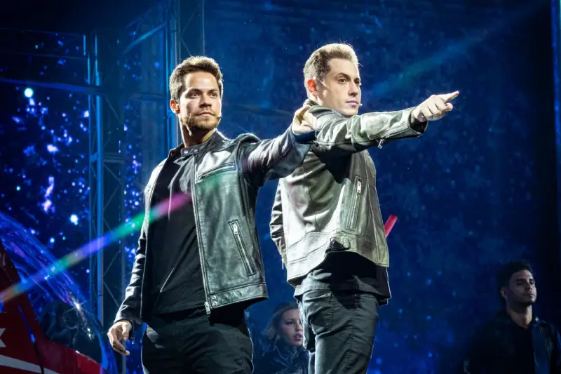 Illusion - Dois ilusionistas em jaquetas de couro em performance no palco com luzes azuis