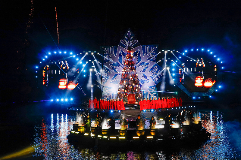 Nativitaten - Cenário aquático com árvore de Natal gigante iluminada sobre a água com fogos de artifício